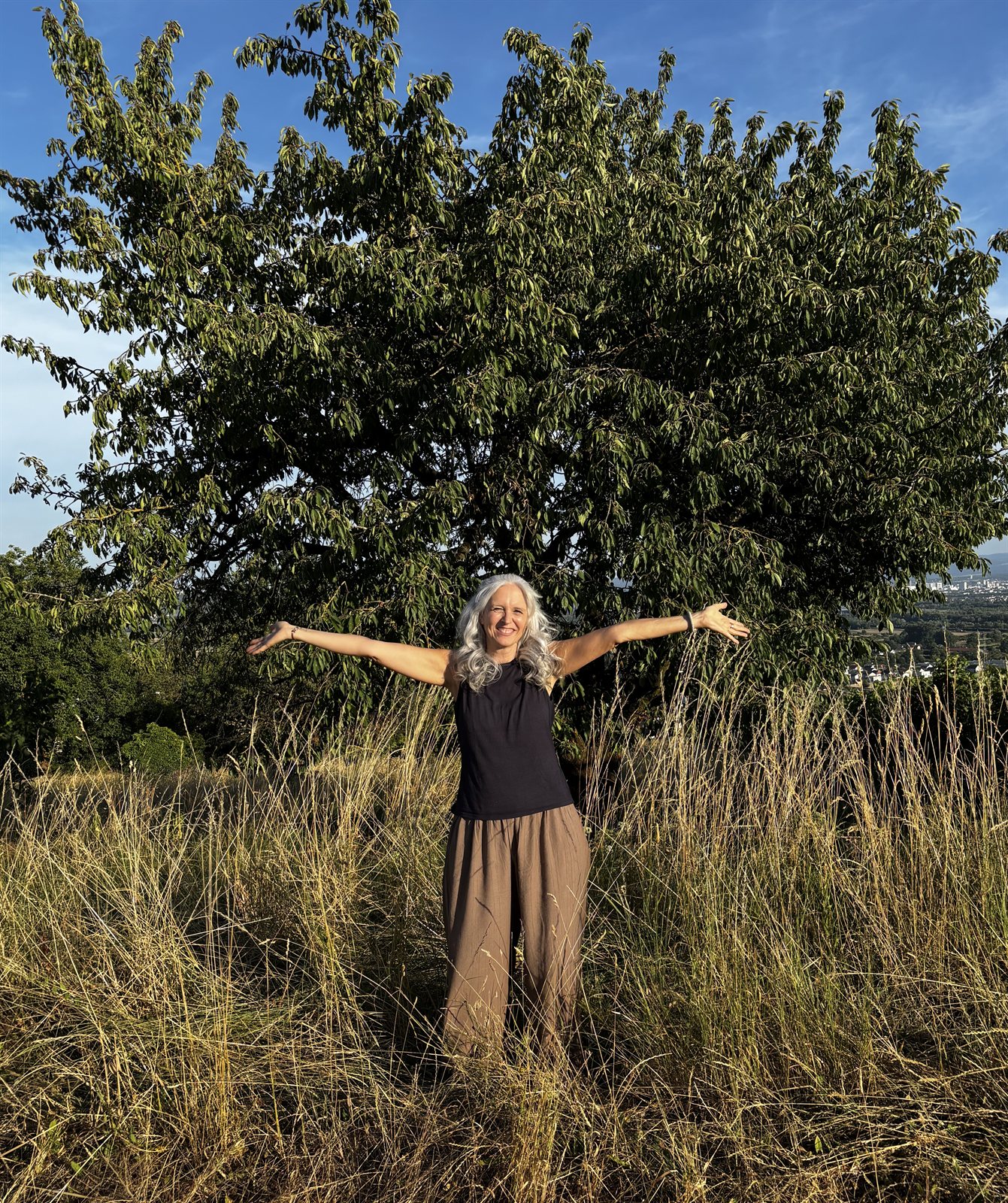 Claudia Pachl mit ausgebreiteten Armen vor einem großen Baum