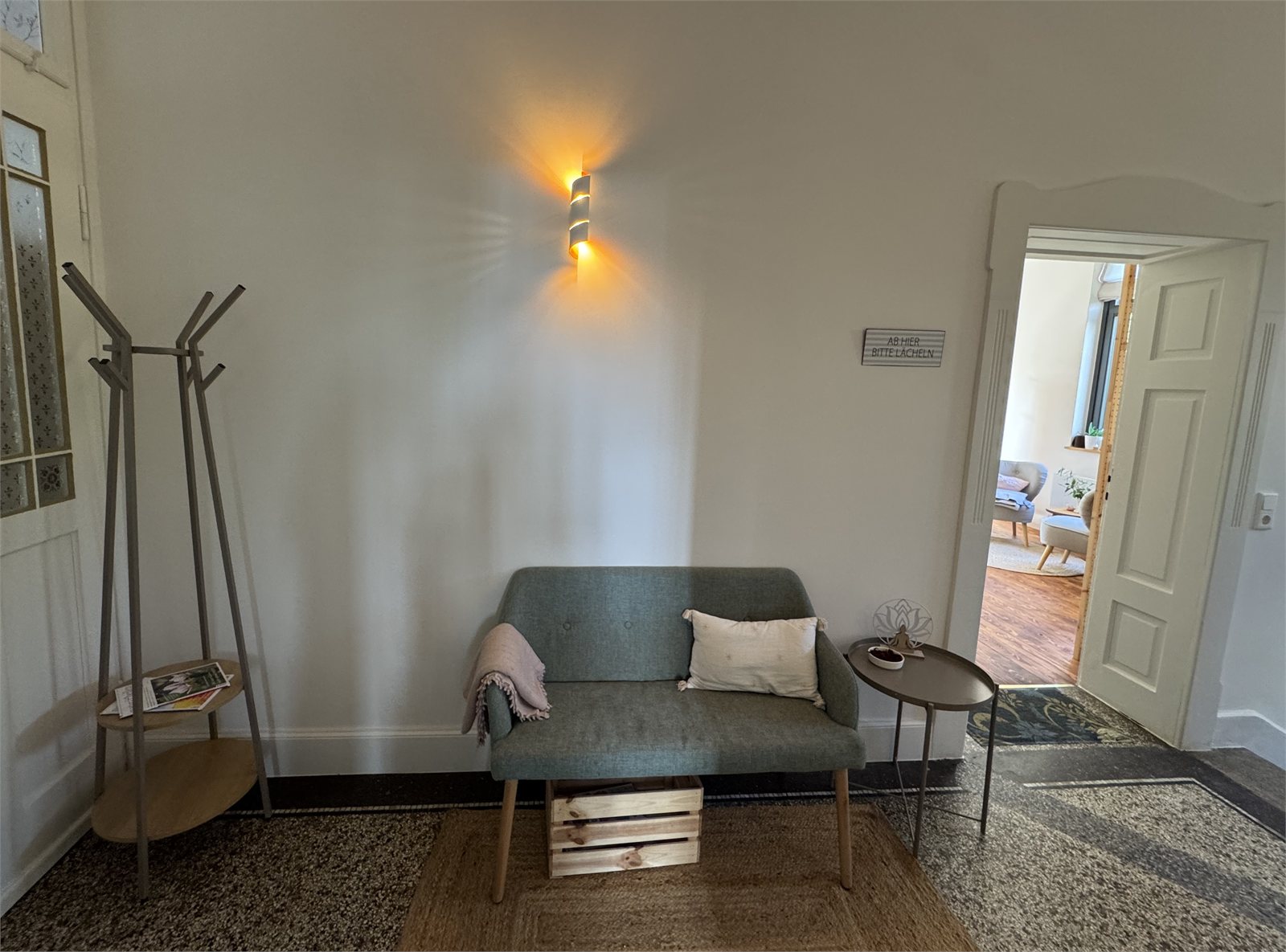 Wartebereich mit Sofa und Garderobe in der Praxis Herz & Hände
